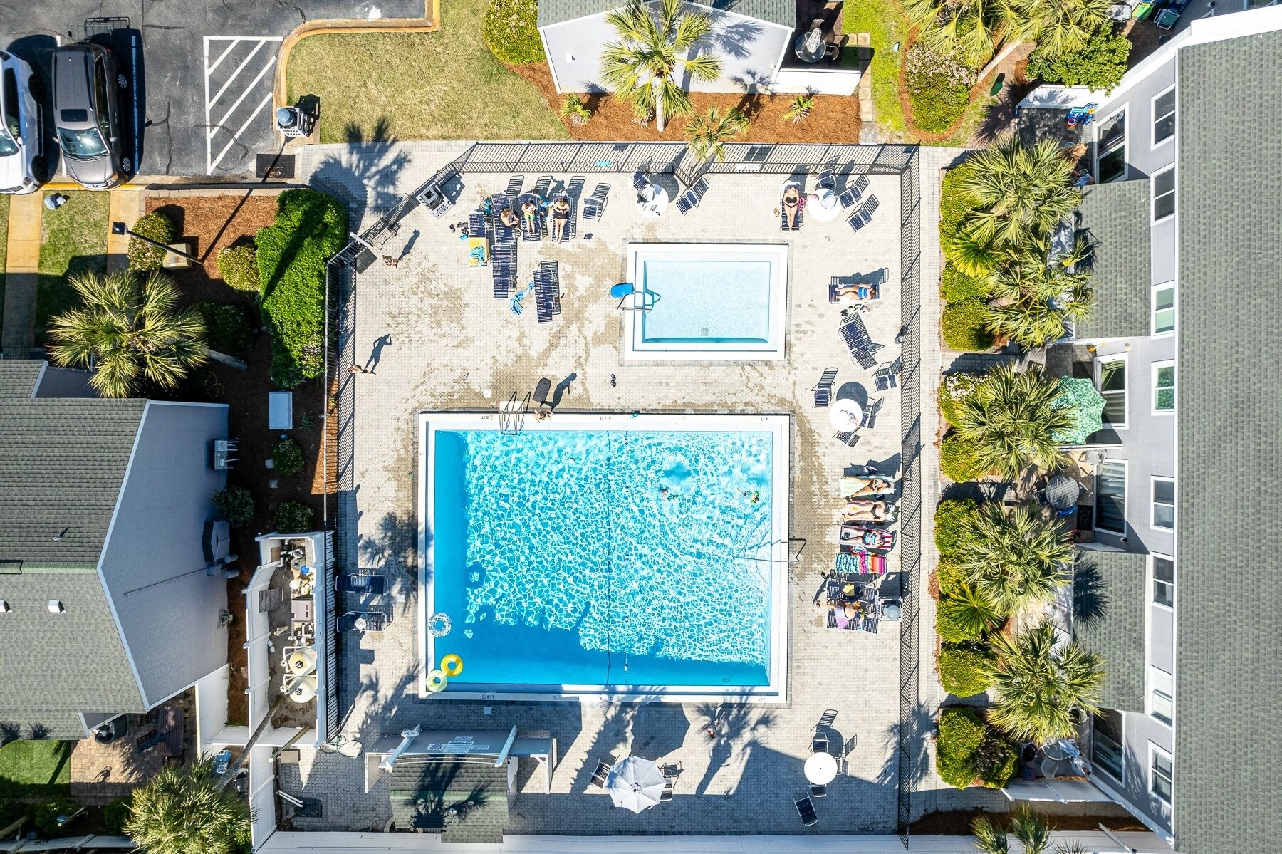 An aerial view of a hotel with a large swimming pool, sun loungers, and palm trees.
