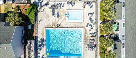 An aerial view of a hotel with a large swimming pool, sun loungers, and palm trees.