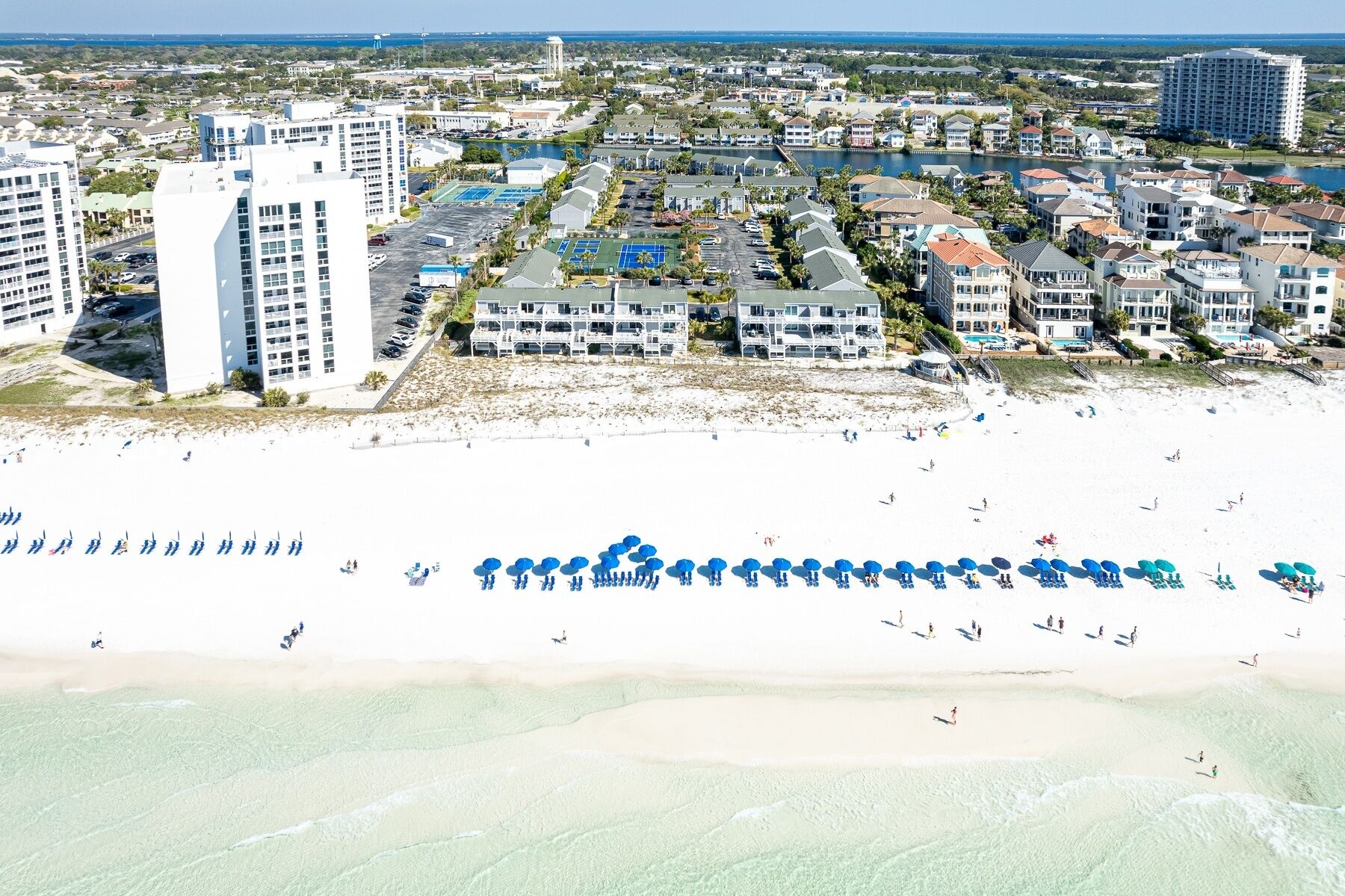 An aerial view of a coastal area with beachfront properties, a sandy beach, and a marina.
