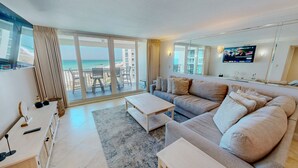 A modern living room with a large sofa, a coffee table, and a TV mounted on the wall. - Shoreline Towers 1052 2 Bedroom Condo by RedAwning (Destin)