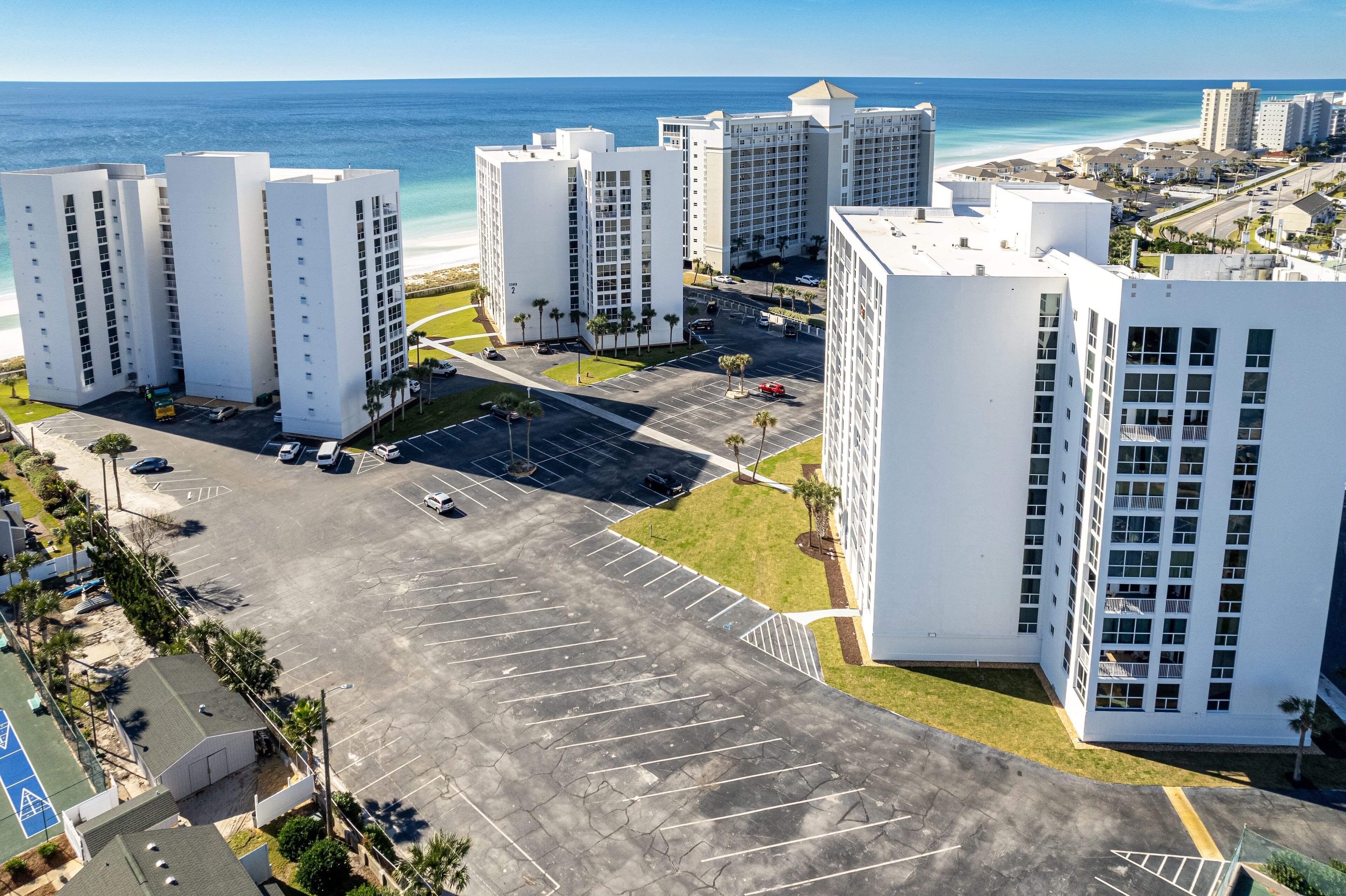 A high-rise hotel with multiple floors, a parking lot, and a view of the beach and ocean.