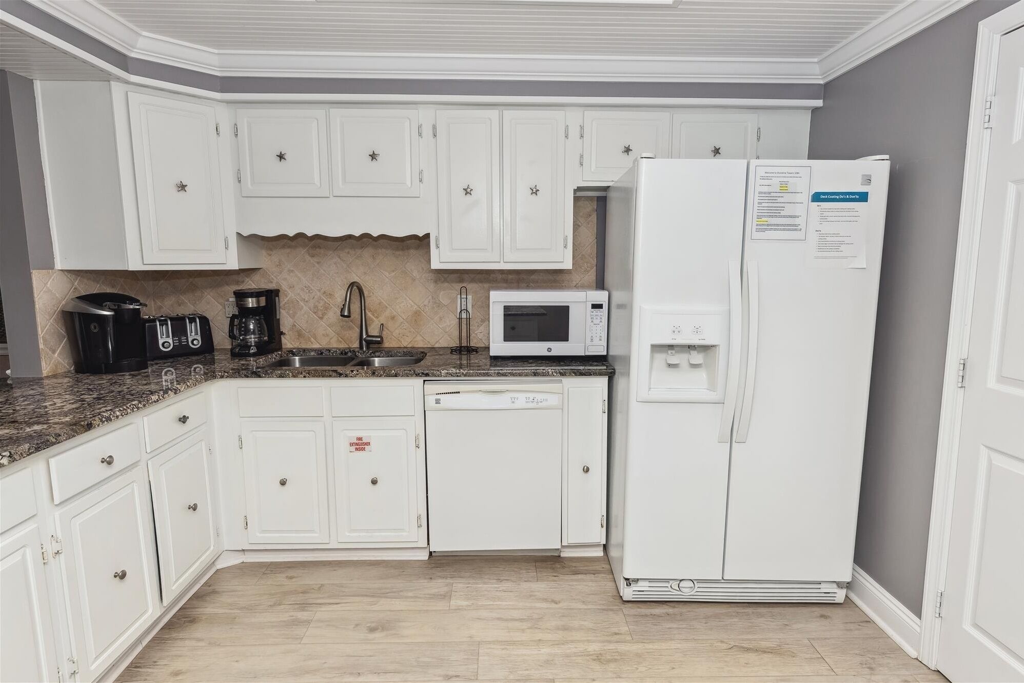 Una cocina con armarios blancos, microondas, cafetera y refrigerador.