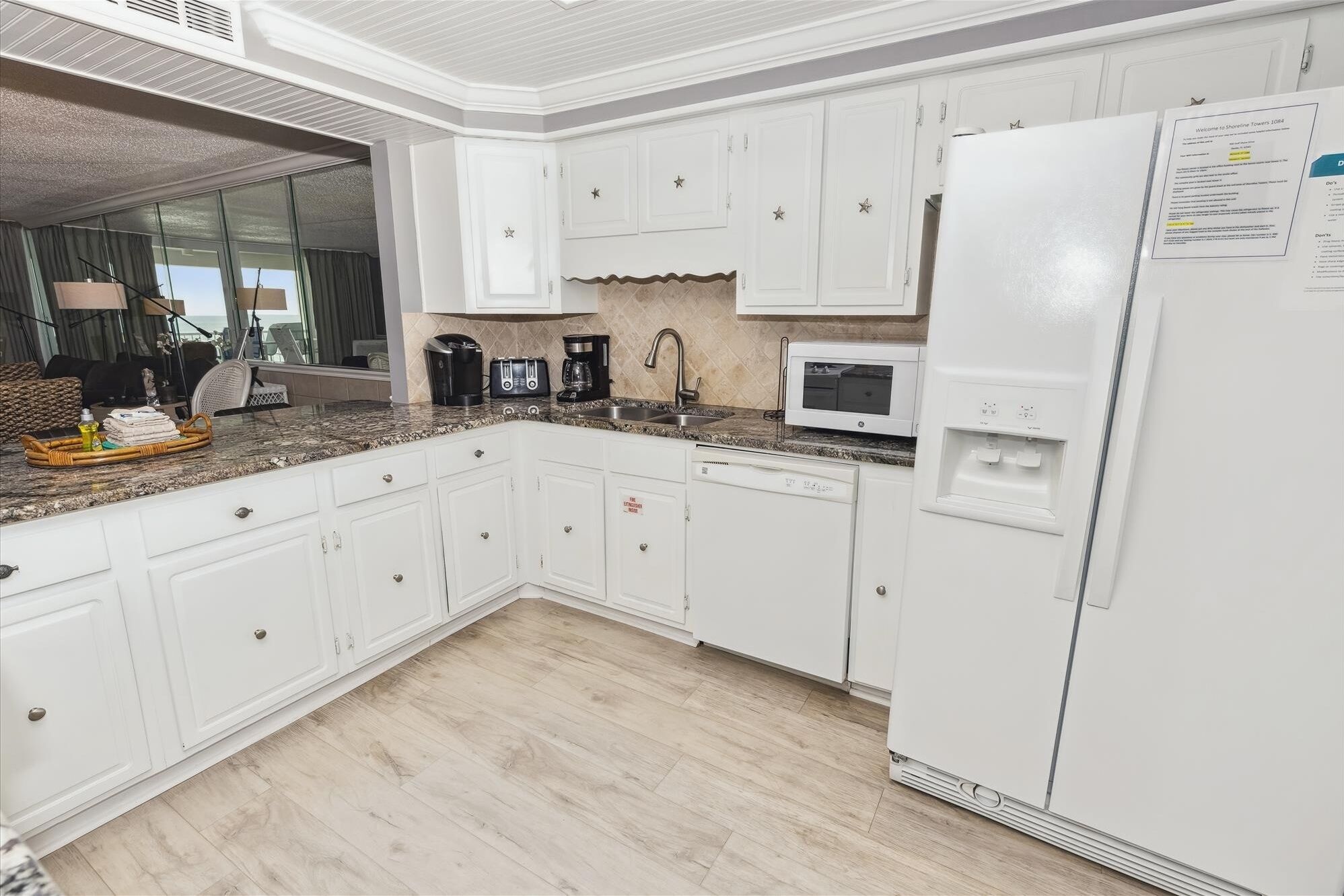 Eine moderne Küche mit weißen Schränken, einer Granitarbeitsplatte, einer Mikrowelle, einer Kaffeemaschine und einem Kühlschrank.