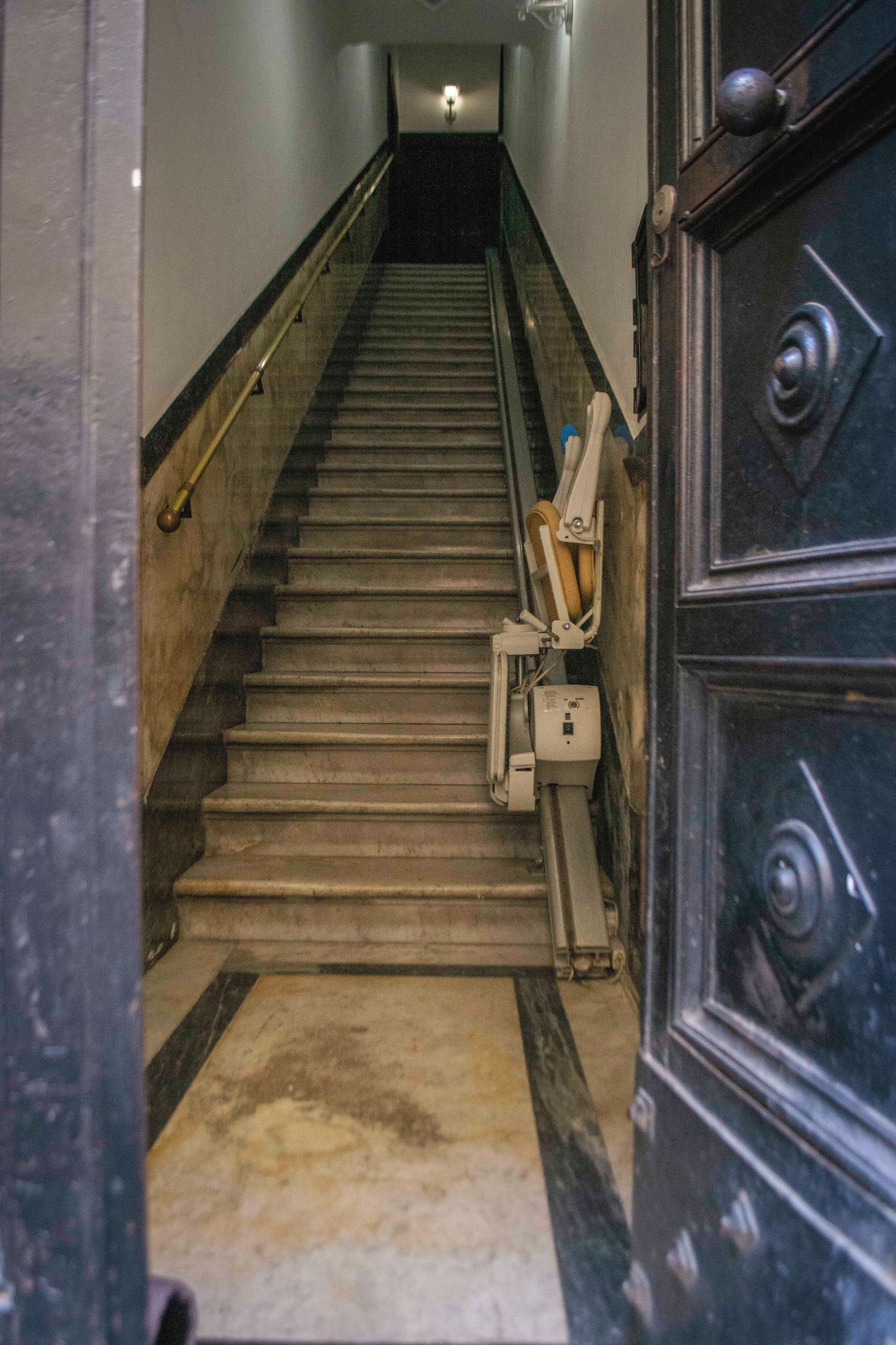 A staircase with a handrail, a chair, and a door with a handle.