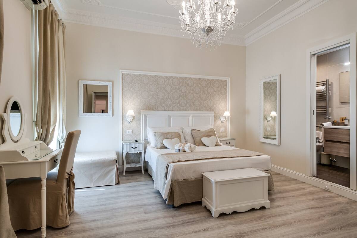 A bedroom with a large bed, a vanity with a mirror, a chandelier, and a walk-in closet.