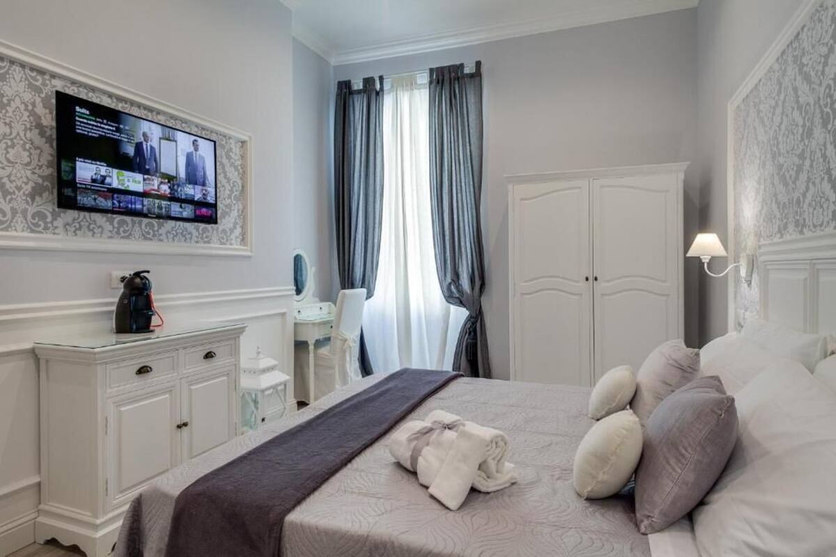 A hotel room with a bed, a television mounted on the wall, a wardrobe, and a desk with a chair.