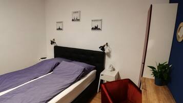 A bedroom with a bed, a nightstand, a red chair, and wall art depicting cities.