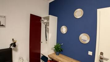 A room with a red door, a white wall with a cityscape poster, a wooden desk with a plant, and a blue wall with decorative plates.