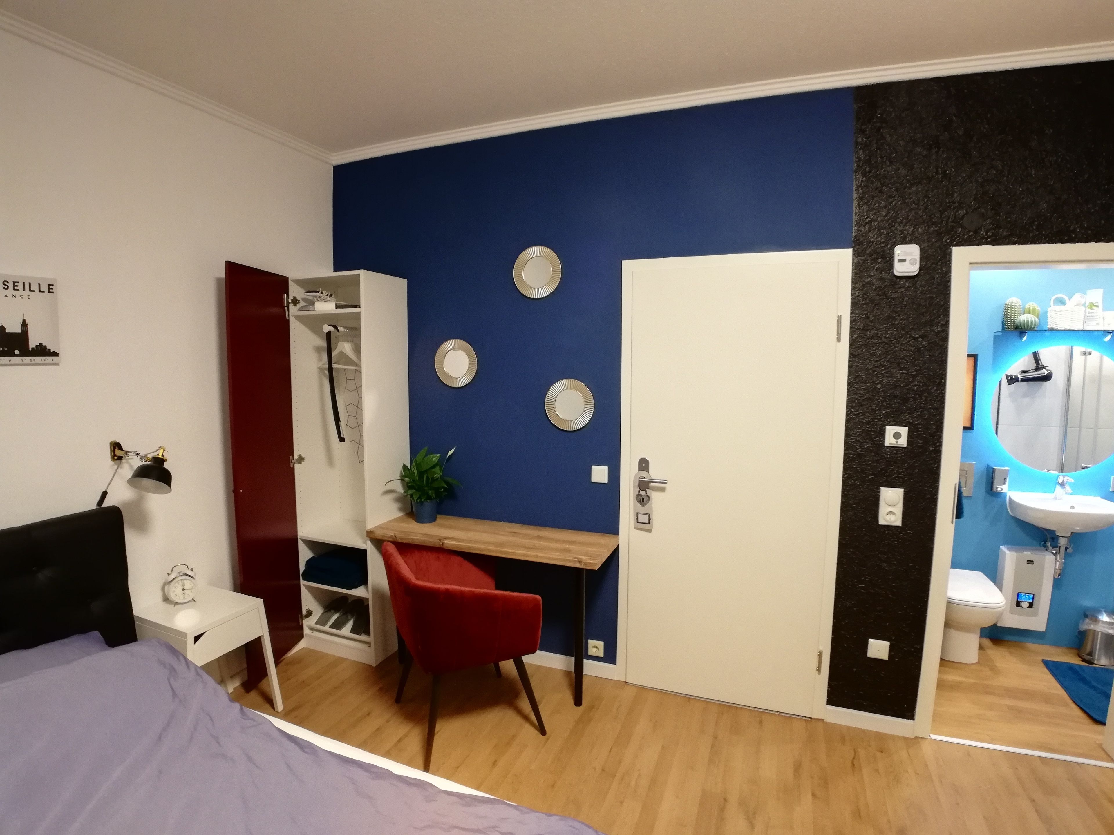 Une chambre à coucher comprenant un lit, un bureau, une chaise, une armoire et une salle de bain avec un lavabo et des toilettes.