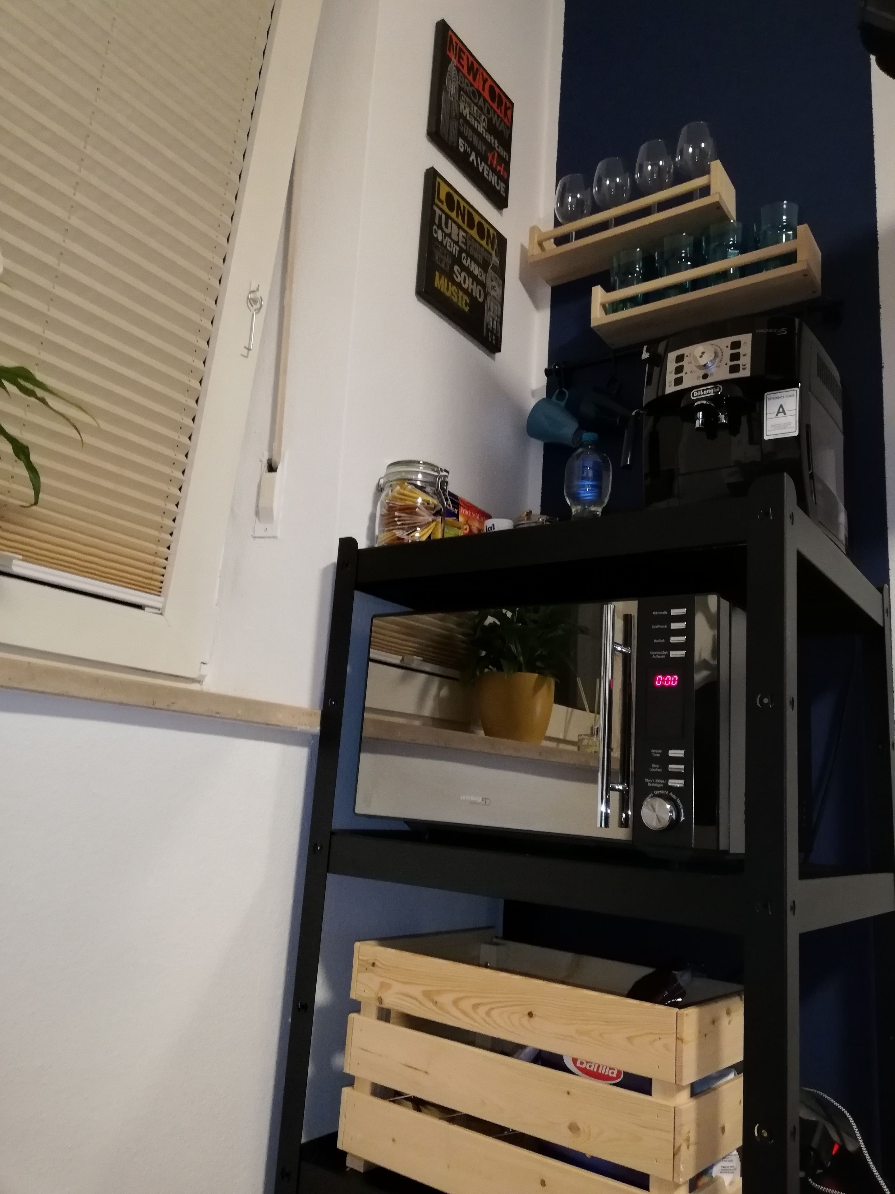 Una cocina con una cafetera, un caja de madera y una estantería con vasos.