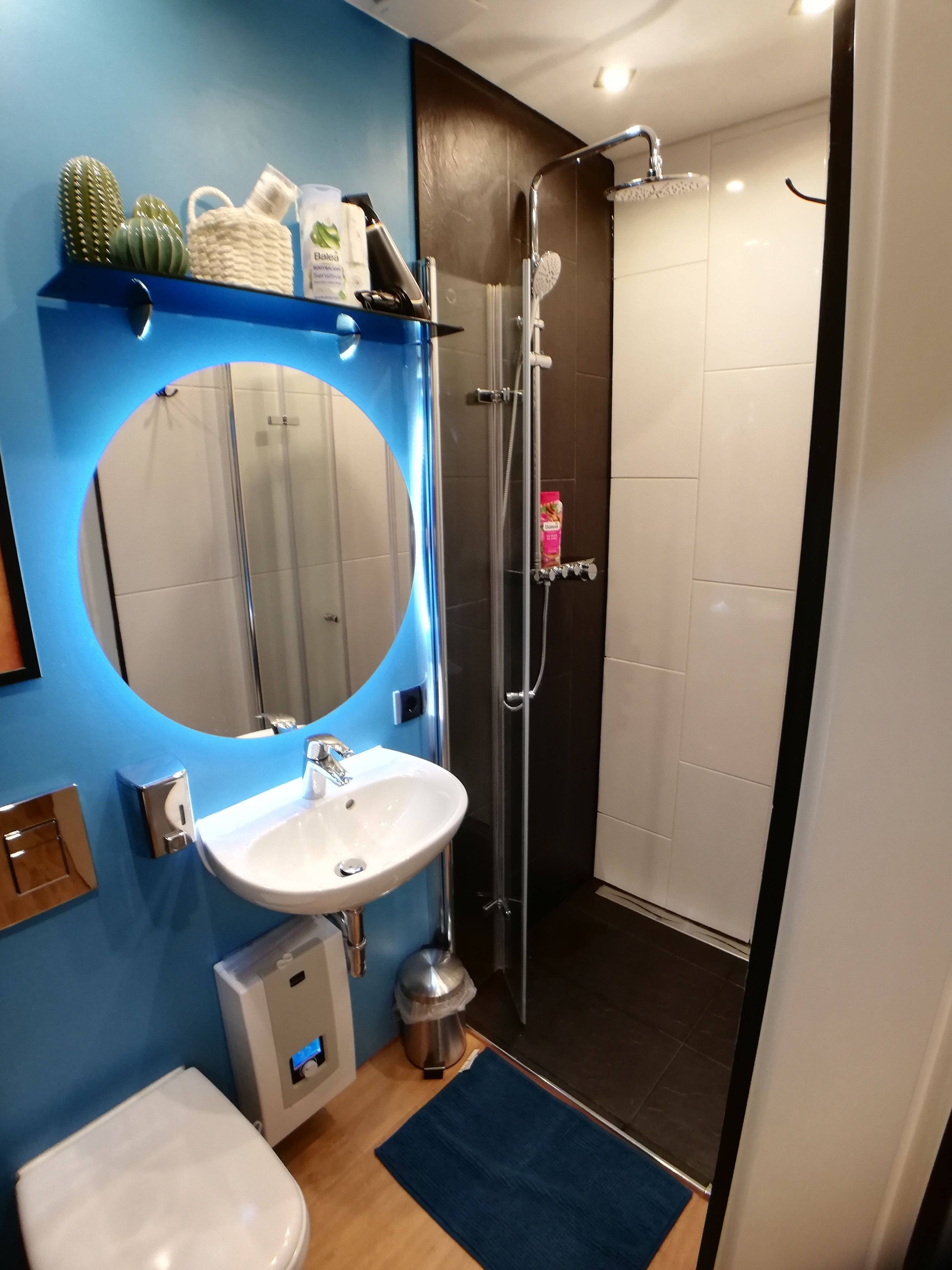 Un baño moderno con un lavamanos blanco, un espejo redondo, una ducha y un inodoro.