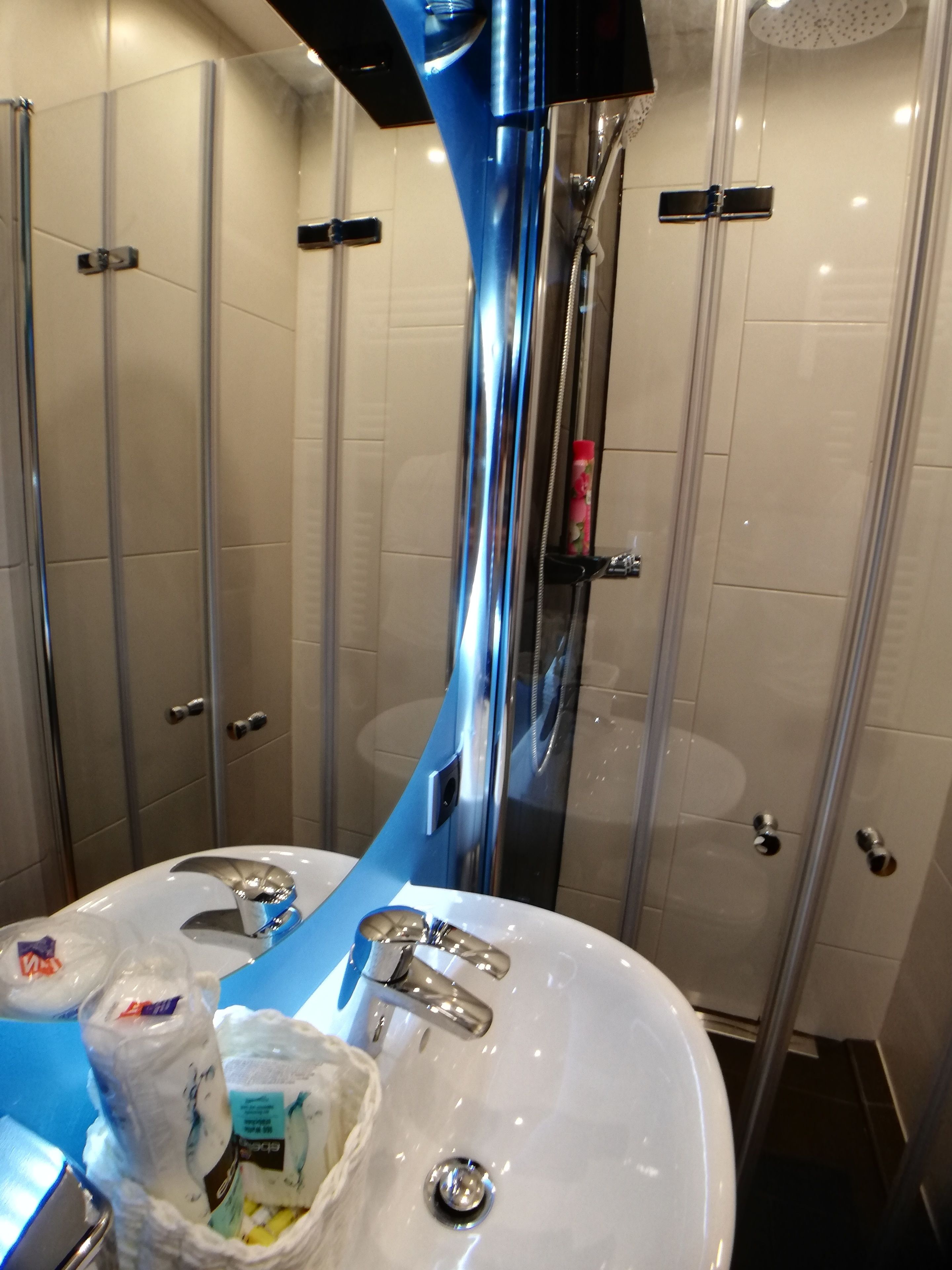 Een moderne badkamer met een douchecabine van glas, een wit wastafelmeubel met chroombeslag en een blauwe accentmuur.