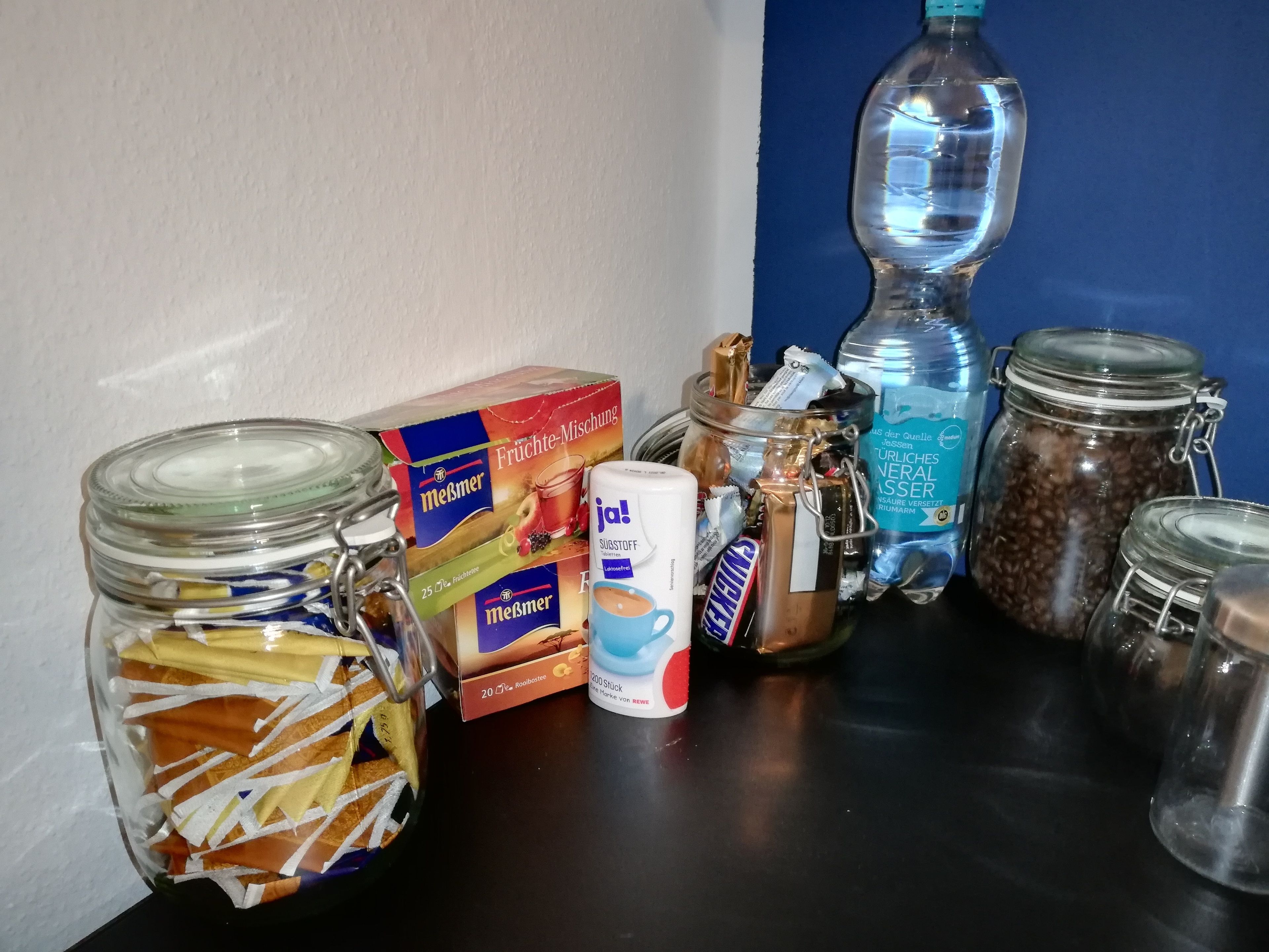 A kitchen counter with various food items and containers, including a box of Meßmer fruit mix, a jar of coffee, and several glass jars.