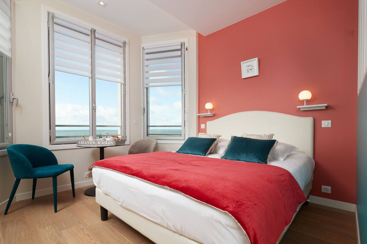 Un dormitorio con una cama, una silla, una mesita y una ventana con persianas.