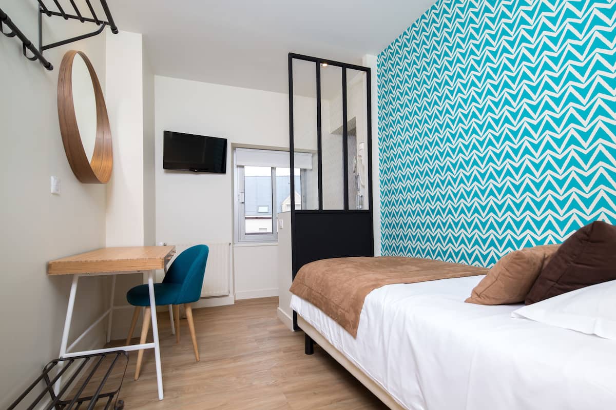 Un dormitorio con cama, escritorio, silla, televisor y pared con diseño.