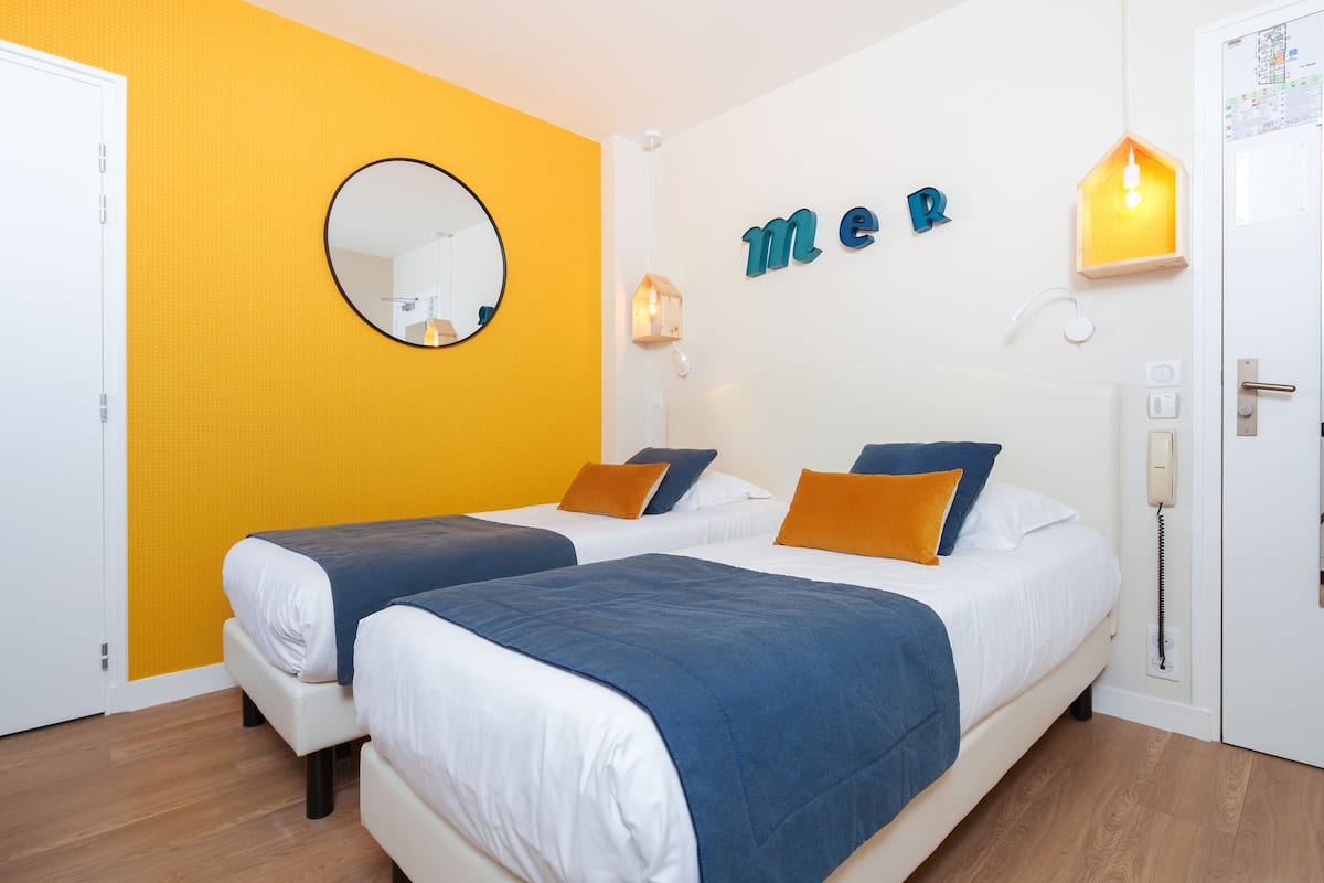 Habitación de hotel con dos camas, un espejo, una lámpara fijada a la pared y una puerta con teléfono.