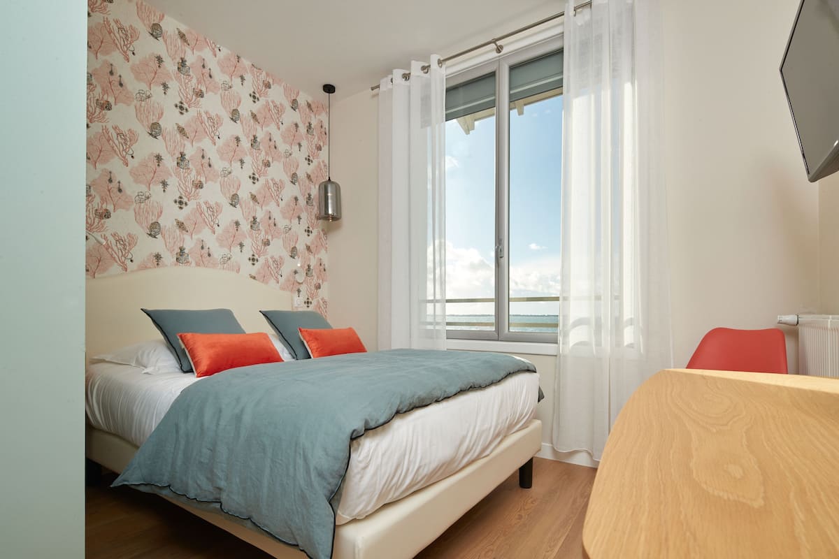 Un dormitorio con cama, una ventana con cortinas, una mesa y un radiador.