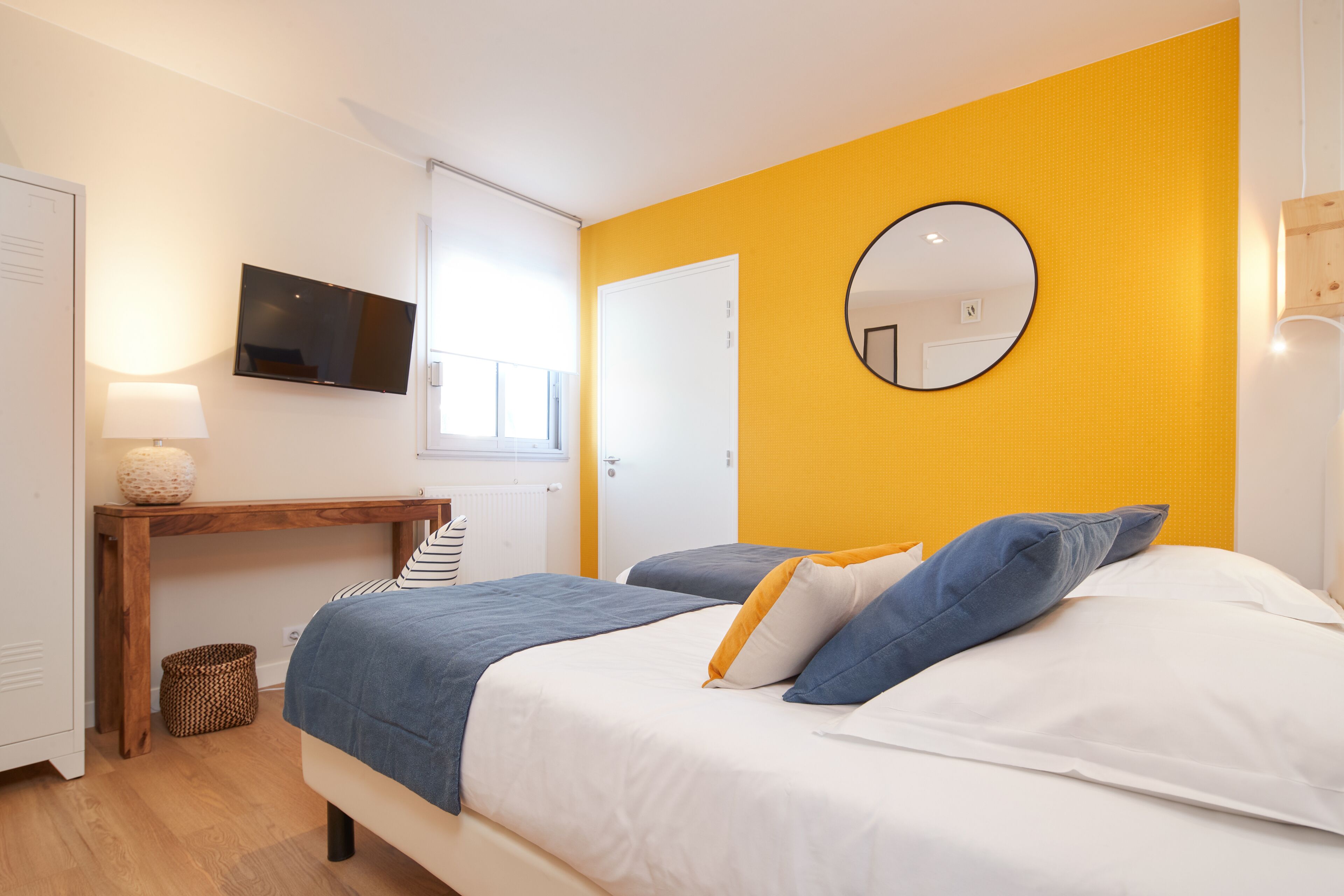 Un dormitorio con cama, mesita de noche, lámpara y televisor en la pared.