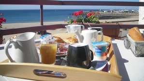 Ontbijttray met theepot, karaf en croissants op een balkon met uitzicht op zee.