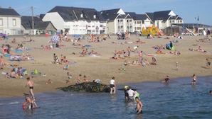 Une plage où l’on voit des gens se prélasser au soleil et nager, avec des bâtiments en arrière-plan.