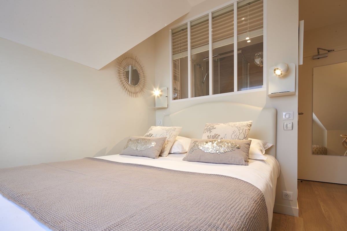 Un dormitorio con una cama grande, una ventana con persianas, un espejo y una lámpara fijada a la pared.