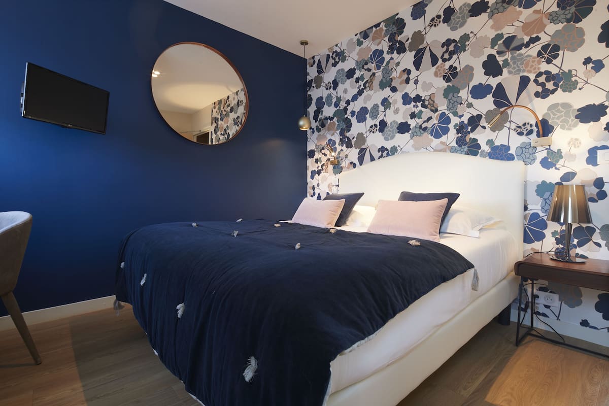 Un dormitorio con cama, espejo redondo, televisor y papel tapiz floral.
