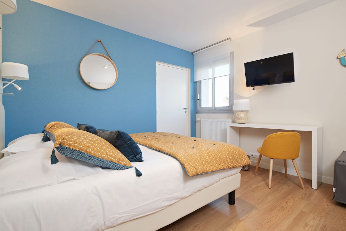 Un dormitorio con cama, escritorio, silla, televisor y espejo.