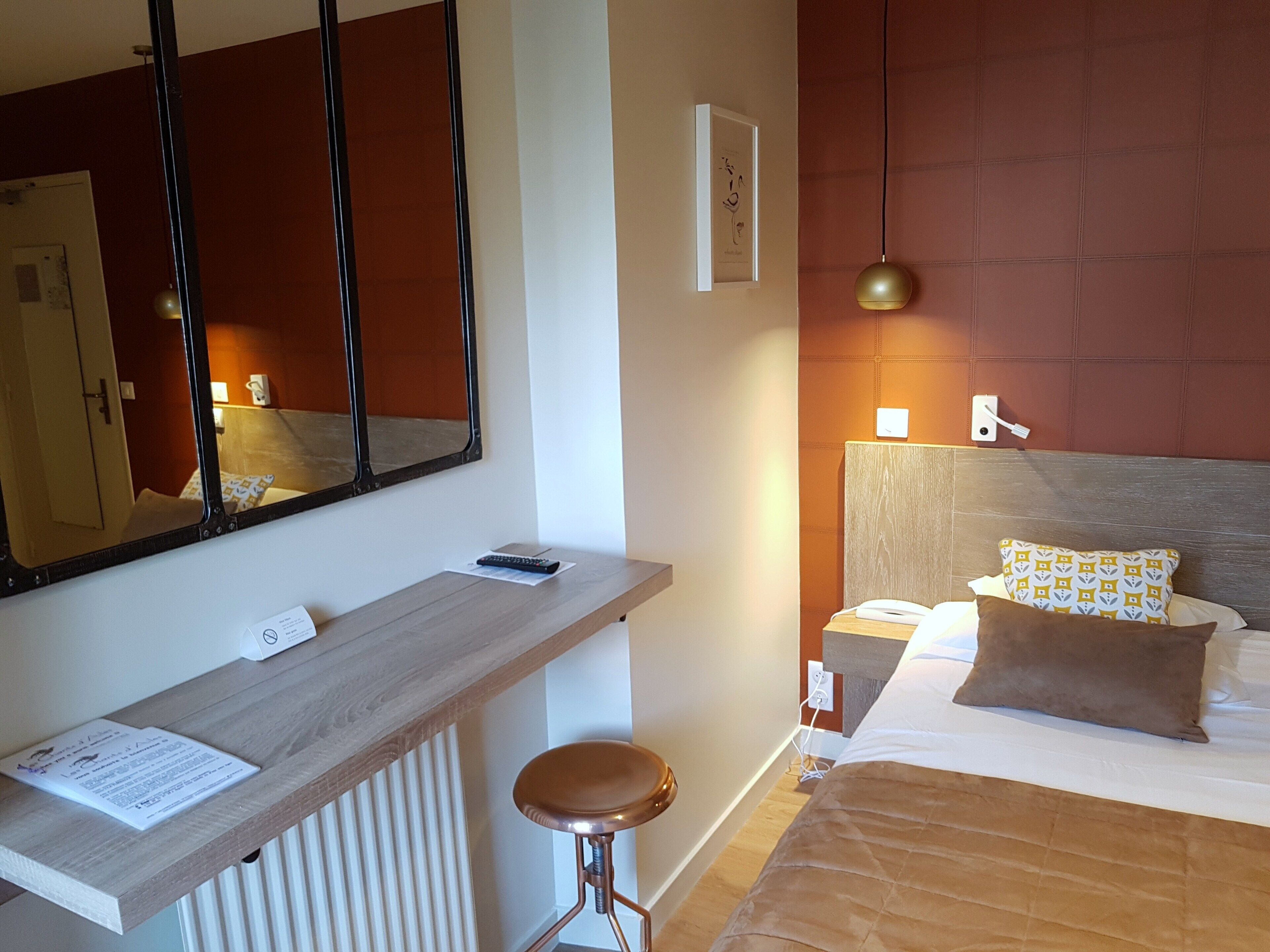 Ein Hotelzimmer mit einem Holztisch, einem Spiegel, einem Bett mit gemusterten Kissen und einer Hängelampe.