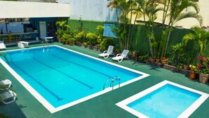 A rectangular pool with two smaller pools, surrounded by green artificial turf, white lounge chairs, and potted plants. - Hotel Payaqui (Esquipulas)