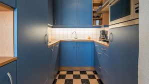 A compact kitchen with blue cabinets, a black and white checkered floor, and stainless steel appliances. - Vitalo 402 (Koksijde)