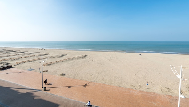 A beach with a paved walkway, a cyclist, and a clear view of the ocean. - Vitalo 402 (Koksijde)