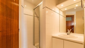 A bathroom with a glass shower enclosure, a white sink, and a wooden door. - Vitalo 402 (Koksijde)