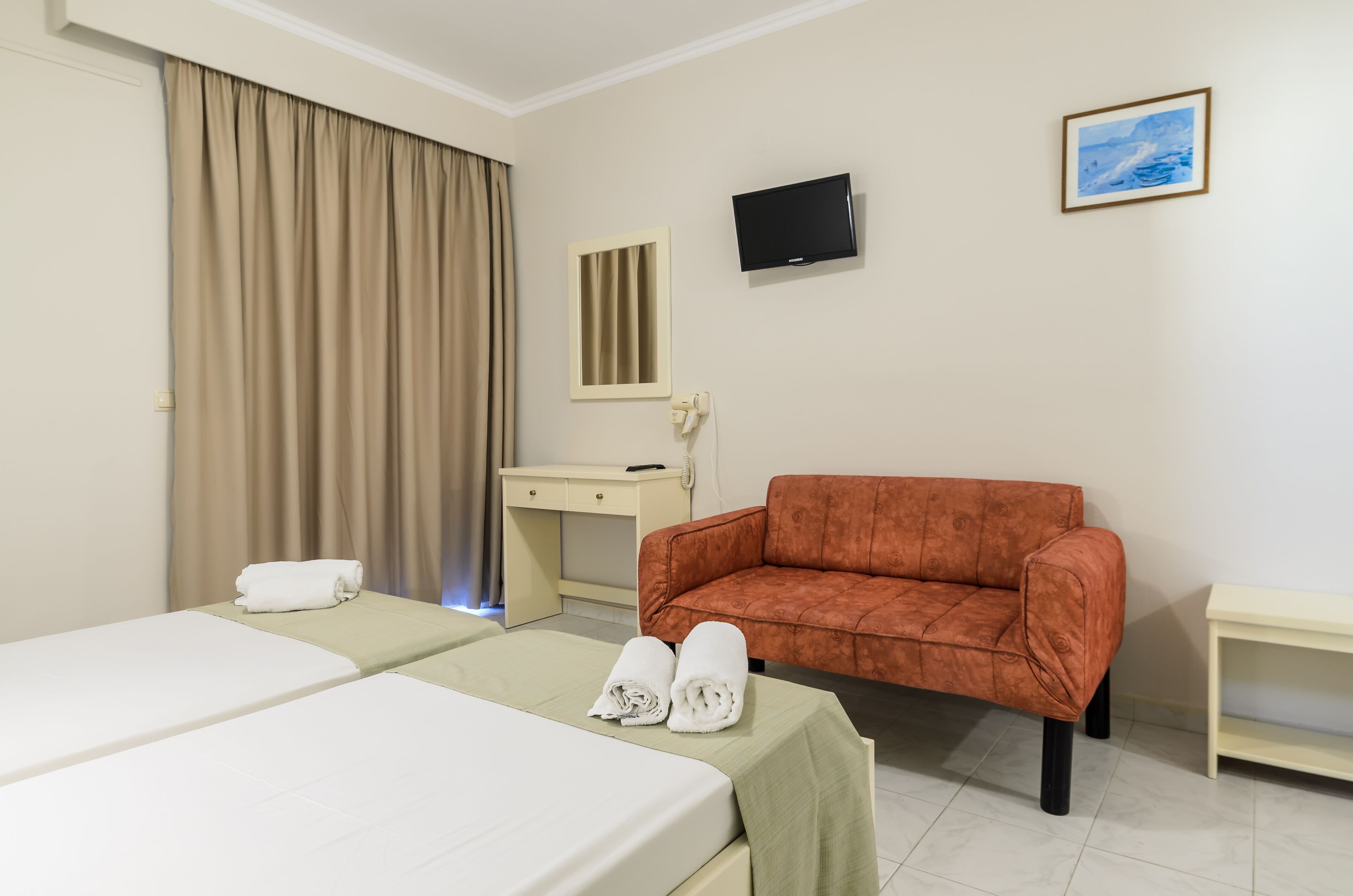 Habitación de hotel con dos camas, un escritorio, un televisor y un sofá.