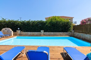 A swimming pool with blue lounge chairs and a stone wall. - Karras Livin (Zakynthos)