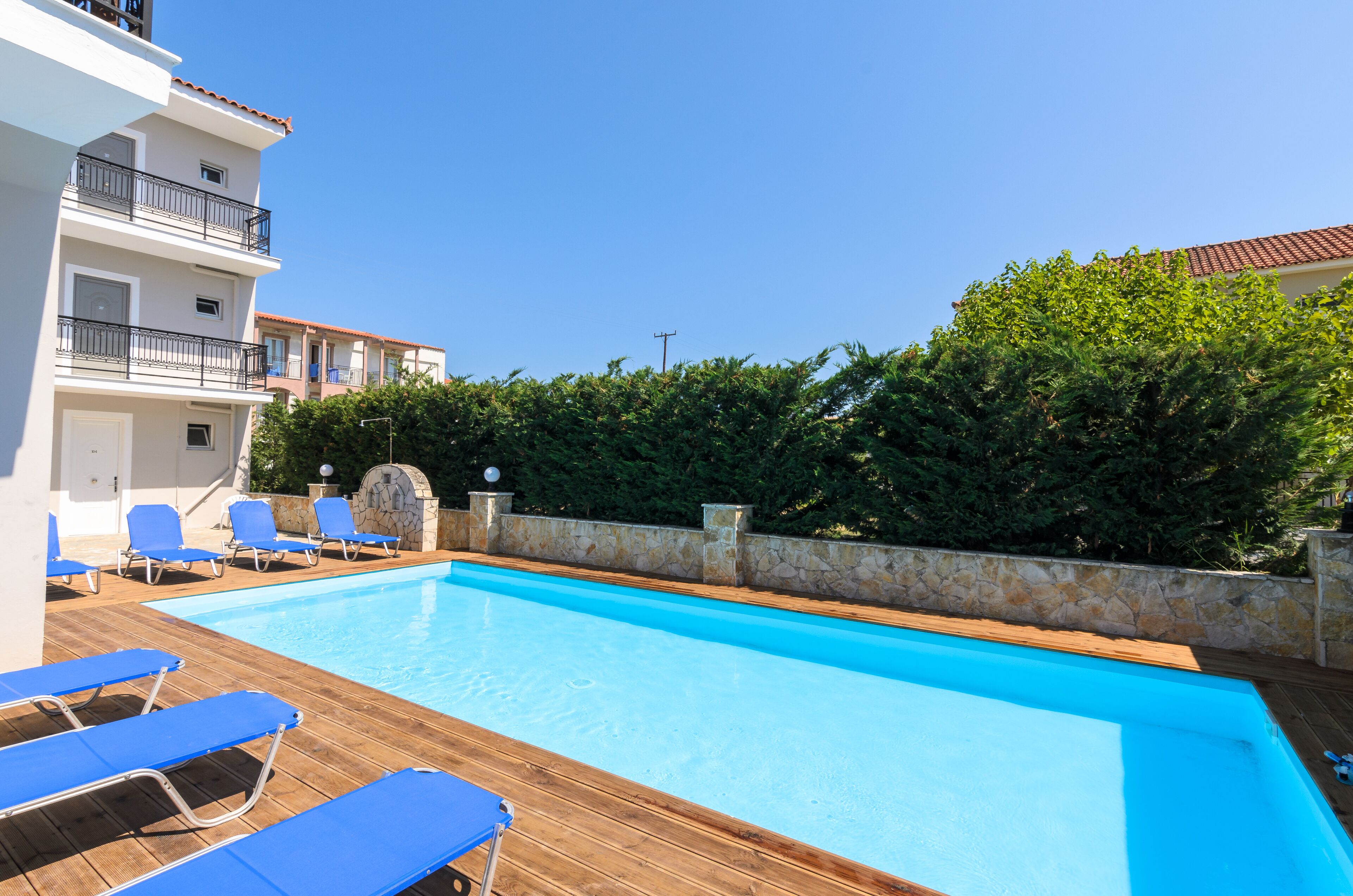 A swimming pool with blue lounge chairs, a stone wall, and a building with balconies.
