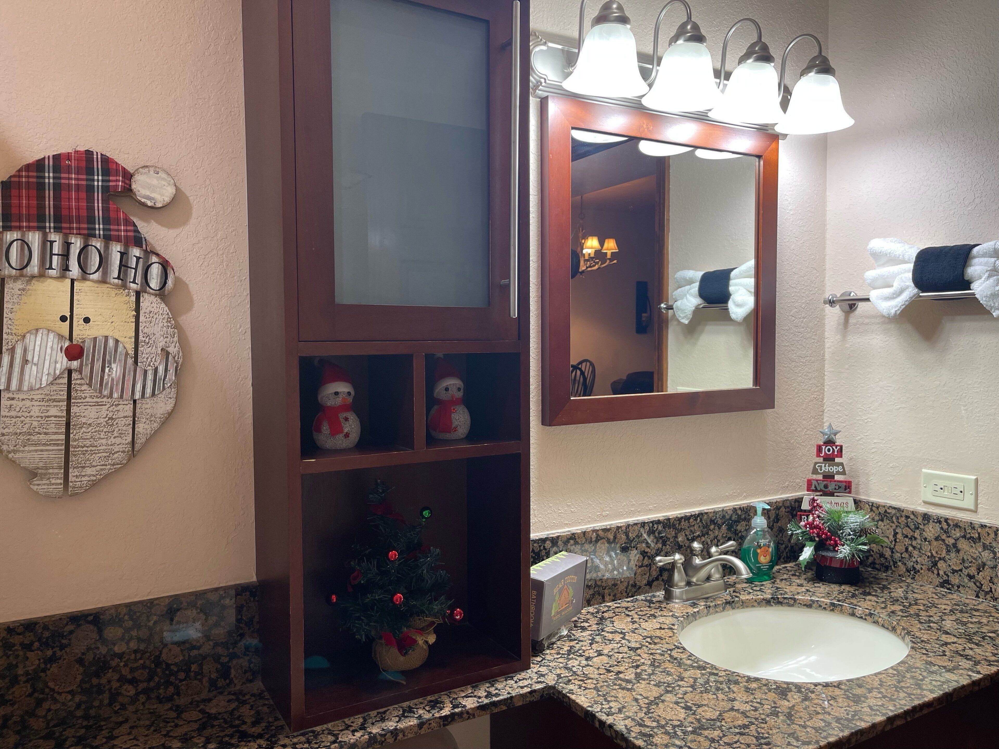 A bathroom with a granite countertop, a sink, a mirror, and a wooden cabinet with a Christmas tree and snowmen decorations.