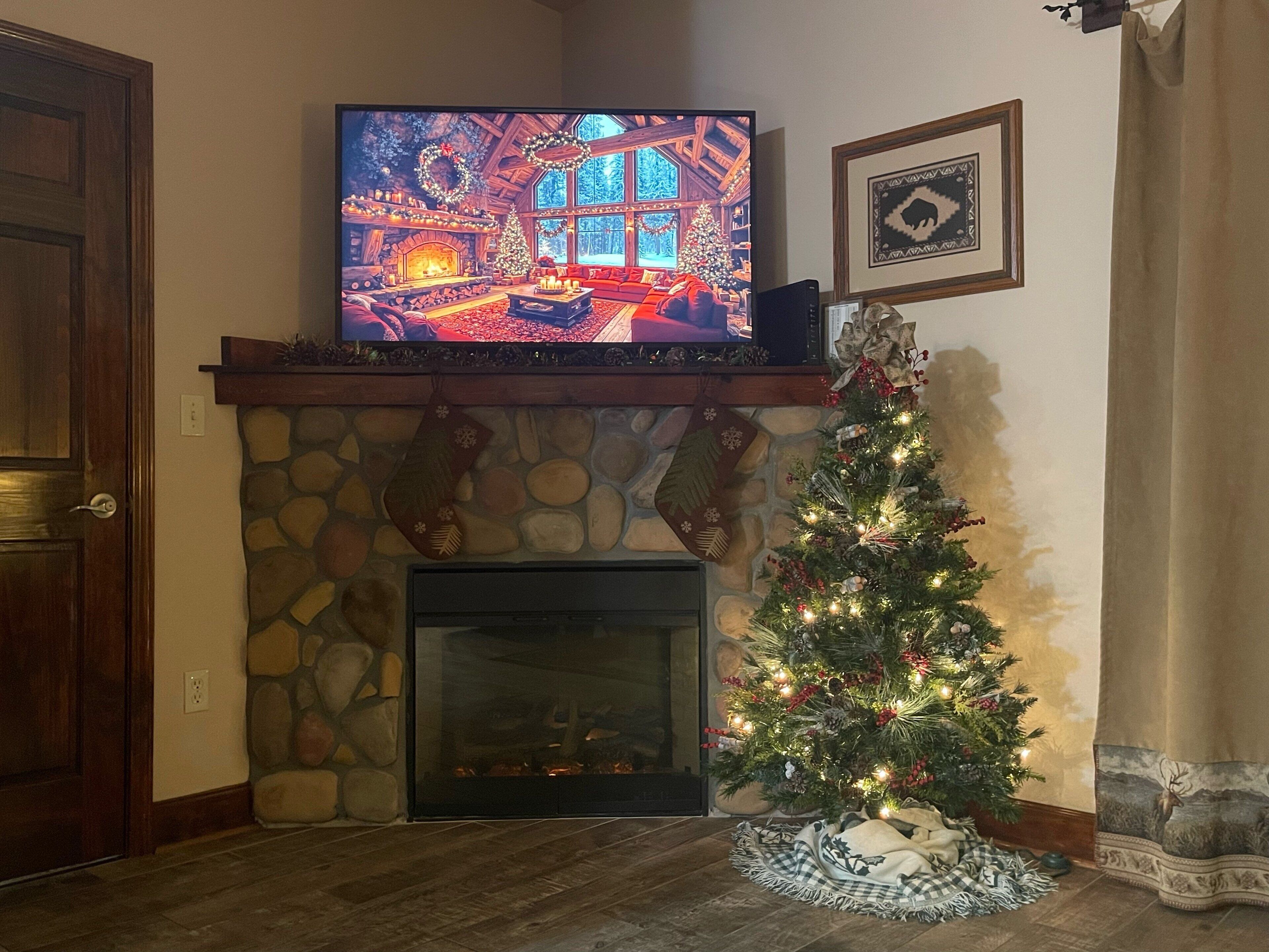 A cozy living room with a fireplace, a Christmas tree, and a television mounted above it.