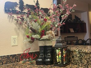 A kitchen counter with a decorative plant arrangement in a boot-shaped vase, a lantern, and a wall-mounted bear silhouette.