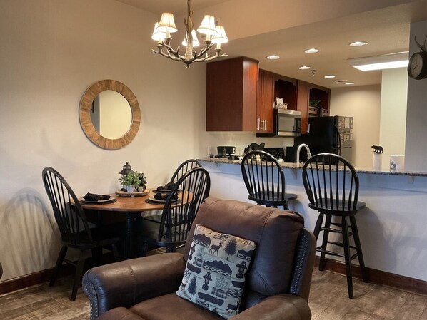 A dining area with a round table, chairs, a chandelier, and a kitchen in the background. - Bearadise Dreams 2 Bedroom Condo by RedAwning (Pigeon Forge)