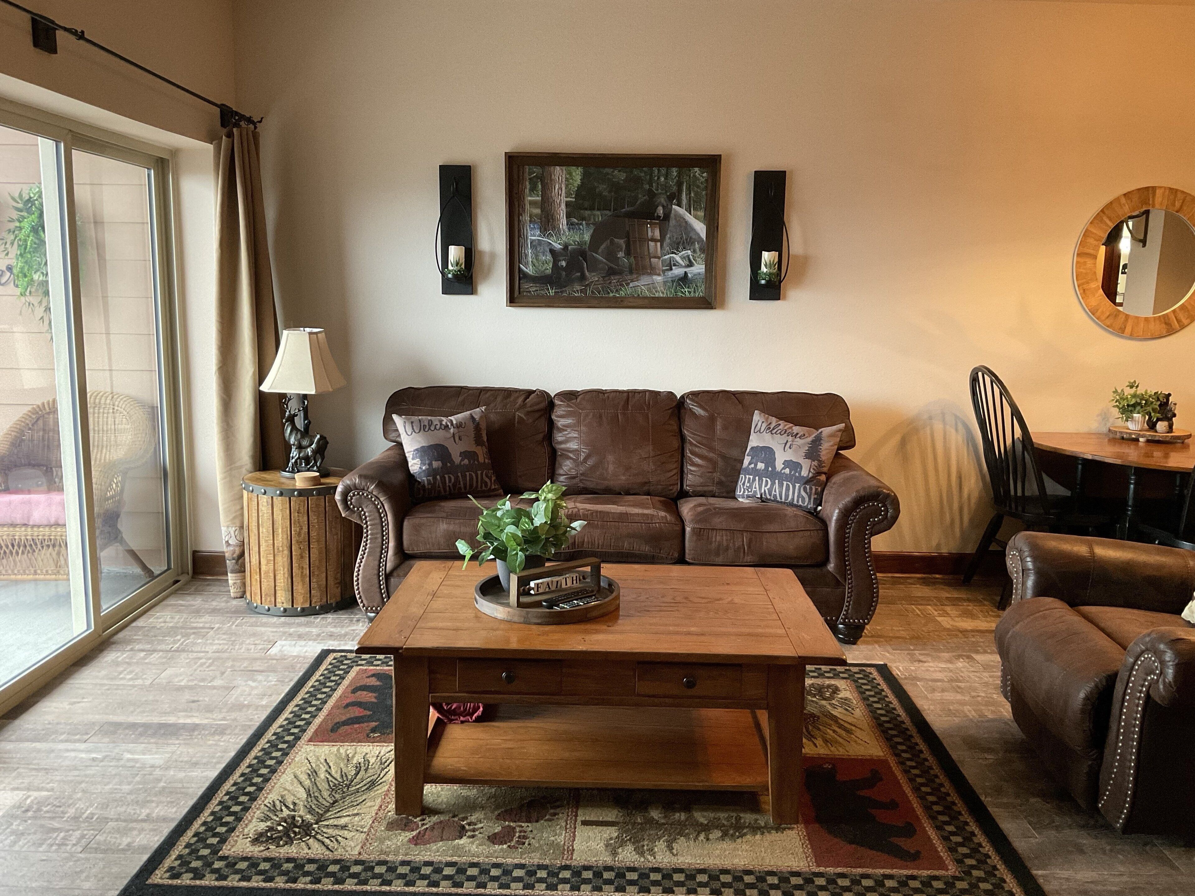Een gezellige woonkamer met een bruine leren bank, een houten salontafel en een kamerkleed met een patroon.