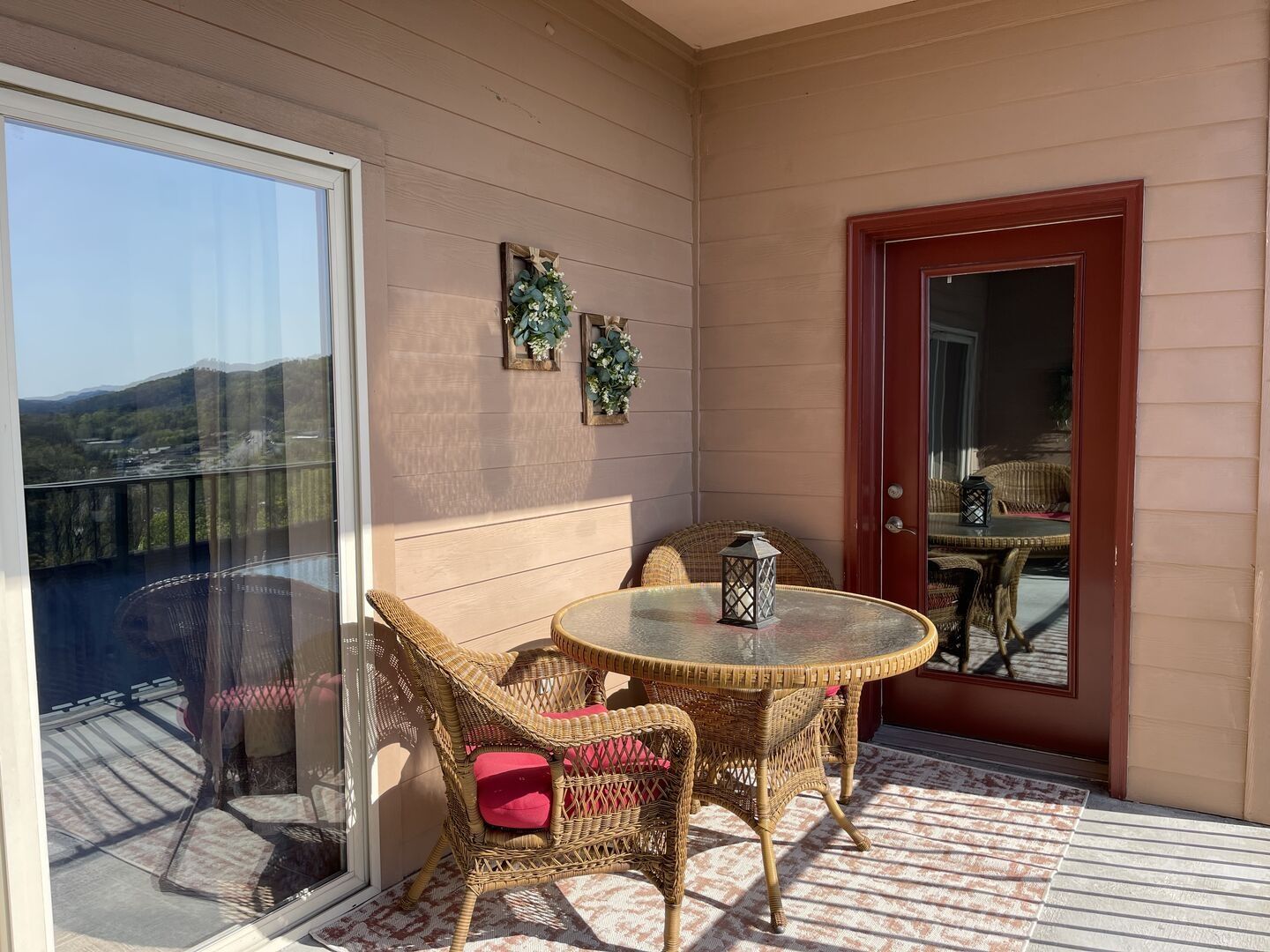En balkon med fletningsmøbler, et glasbord og en dør med udsigt over landskabet.