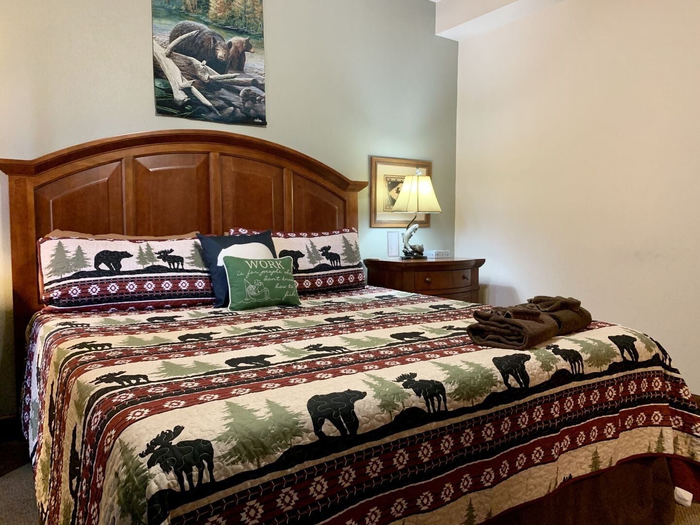 Un lit recouvert d’une couvre-lit à motifs représentant des silhouettes d’animaux, un oreiller orné d’une citation inspirante et un tableau représentant un ours, accroché au mur.