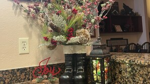 Eine Küchenarbeitsplatte mit einer dekorativen Pflanzenanordnung, einem Paar Stiefel und einem Laternenleuchter.
