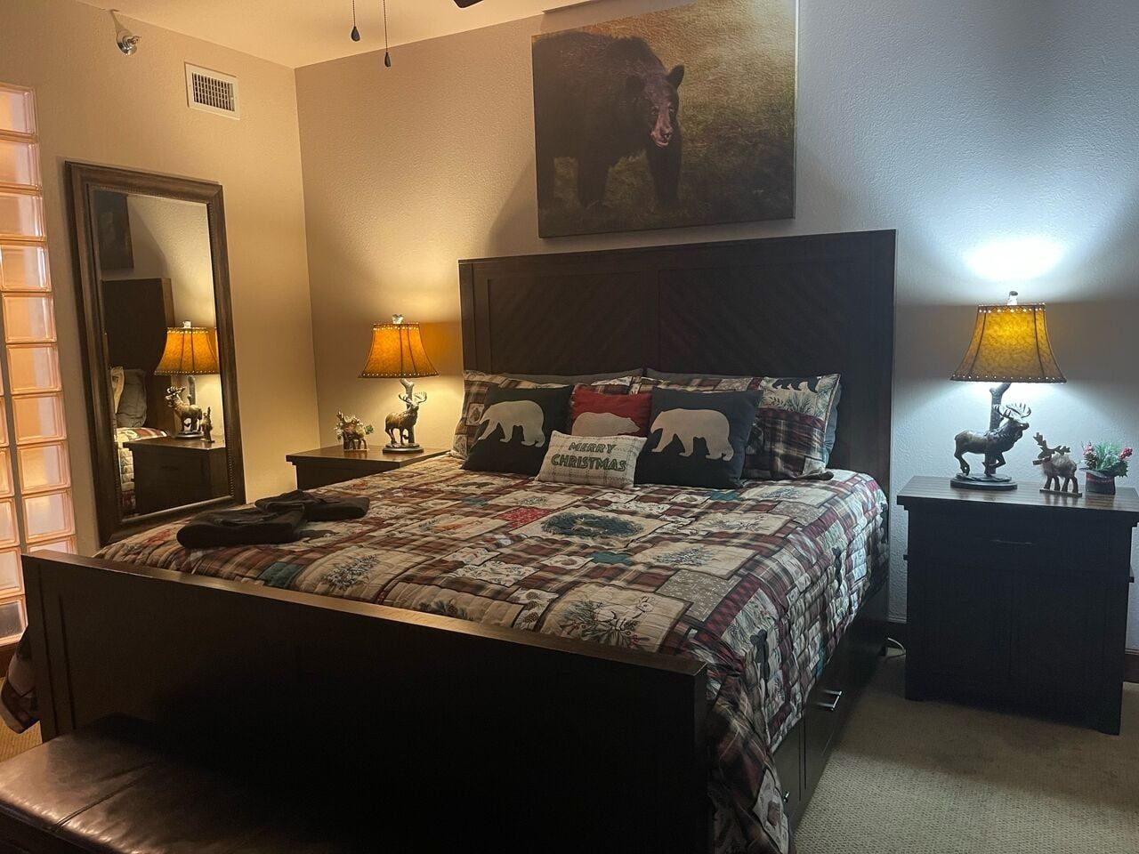 A bed with a quilt, two bedside lamps, a mirror, and a wall-mounted painting.