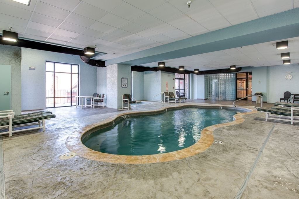 Une piscine intérieure au design incurvé, entourée d’espaces aménagés pour s’asseoir et dotée d’un sol carrelé.