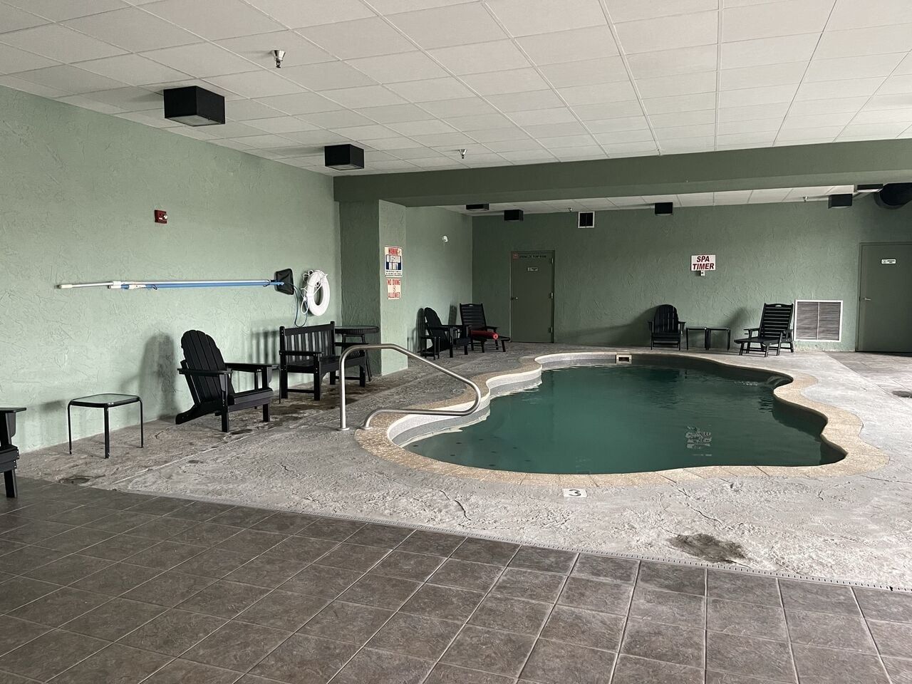 An indoor swimming pool with a tiled floor, lounge chairs, and a spa timer sign.
