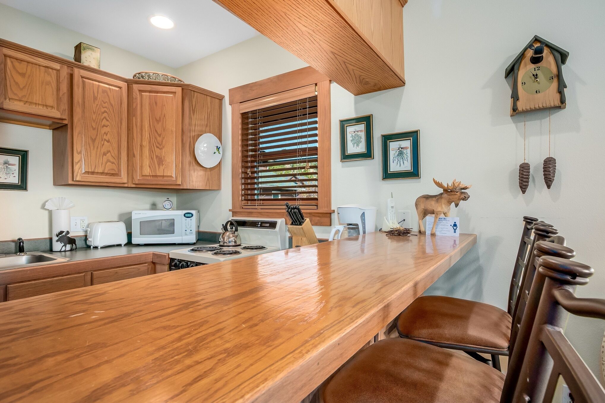 A kitchen with wooden cabinets, a wooden countertop, a microwave, a toaster, and a clock.