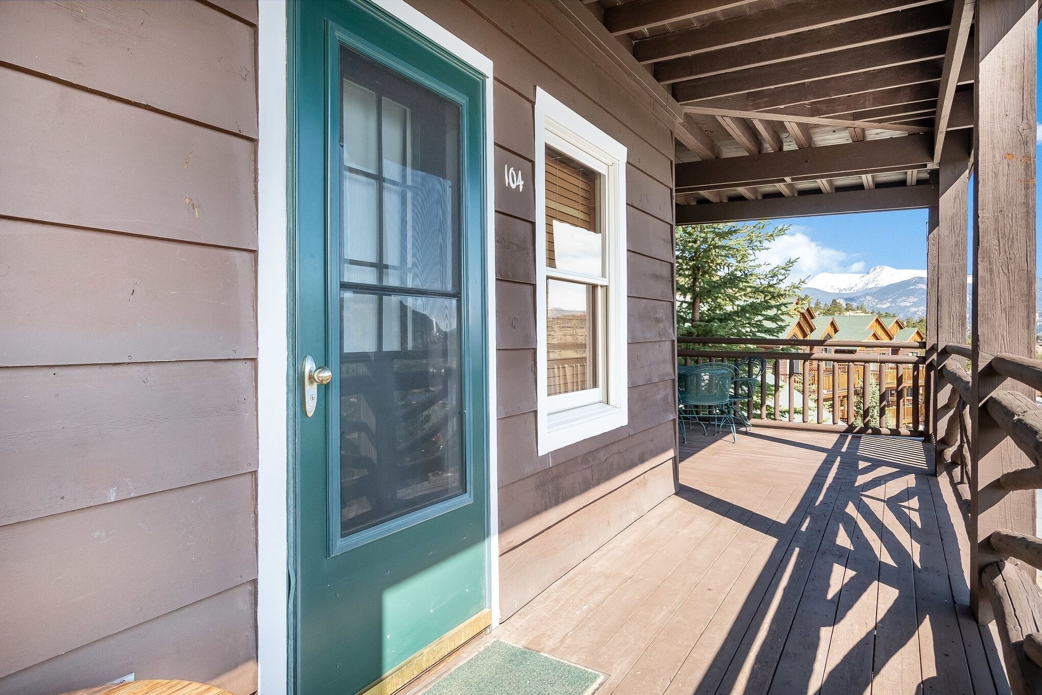 A wooden porch with a green door and a number 104 on the wall.