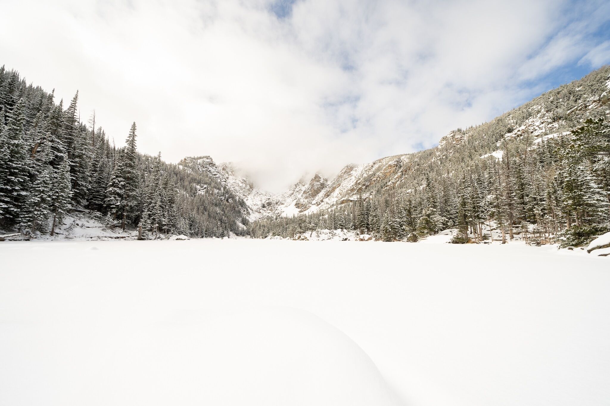 A snowy mountain landscape with dense forests and a clear sky.