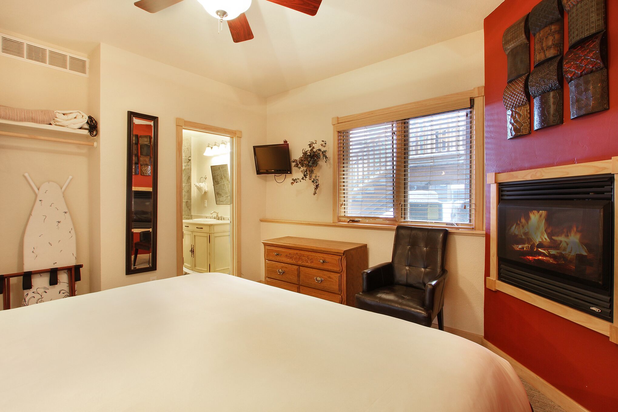 A bedroom with a bed, a wooden dresser, a chair, a television, and a fireplace.